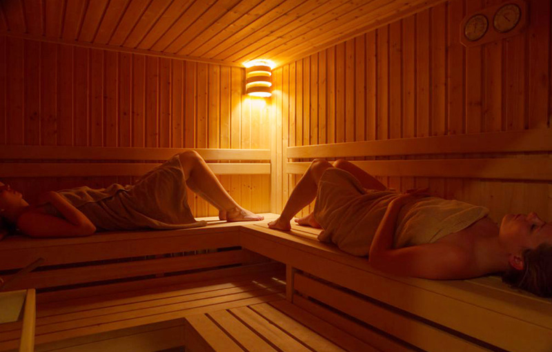 Two women lying down in a wooden sauna.