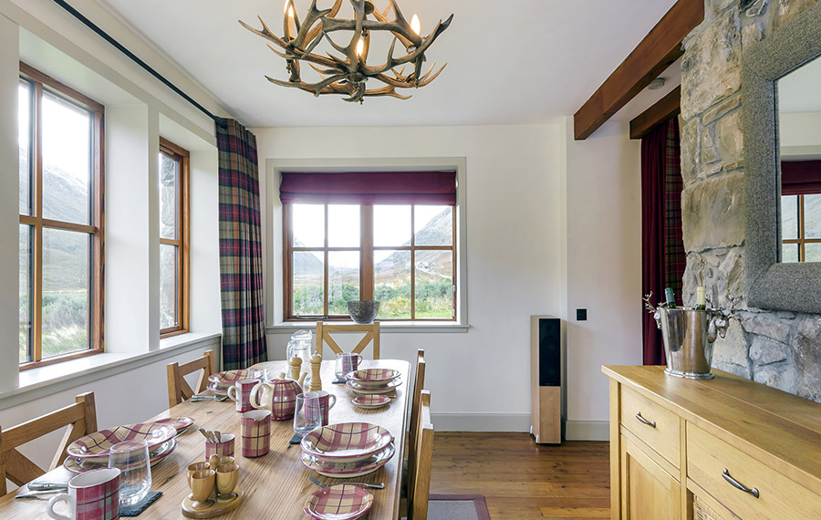 Spacious dining room including large wooden table, set with tartan tableware.