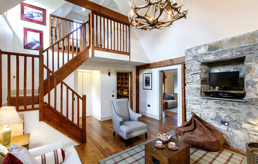 Rustic living room with stone wall, small TV, plentiful seating and wooden staircase.