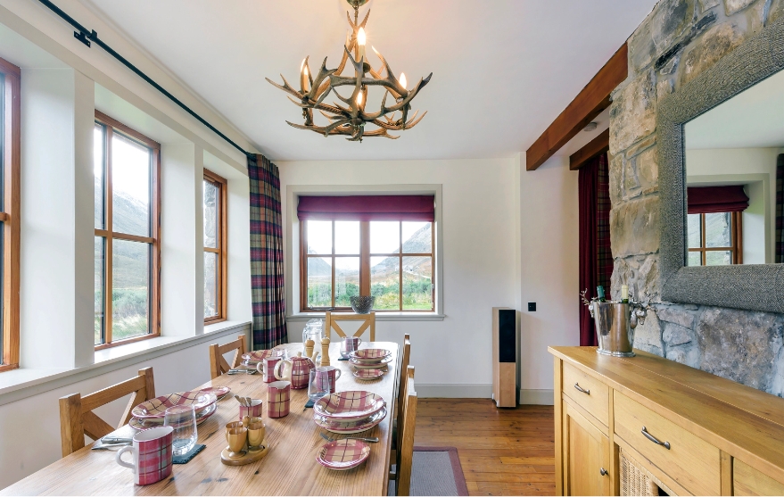 Spacious dining room including large wooden table, set with tartan tableware.