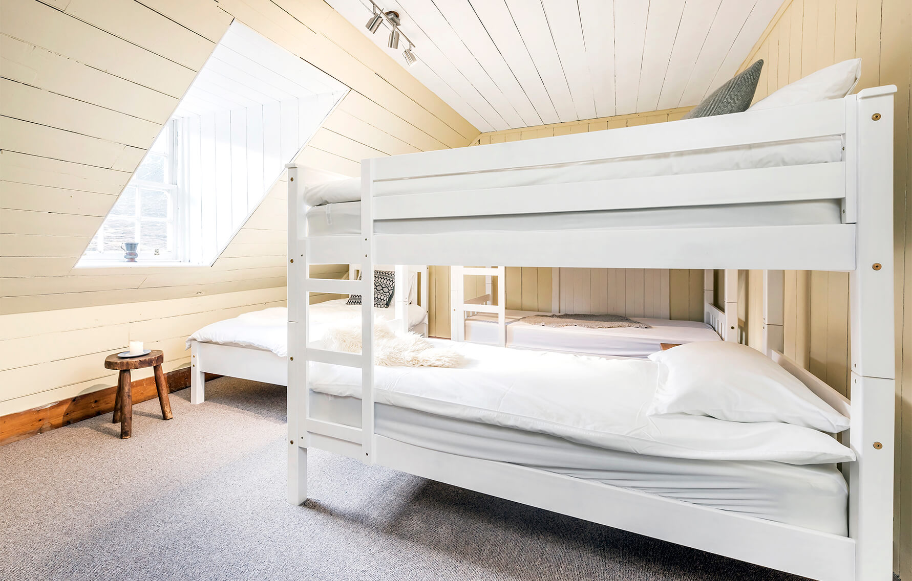 Bright panelled bedroom including two sets of white wooden bunkbeds alongside a single bed.