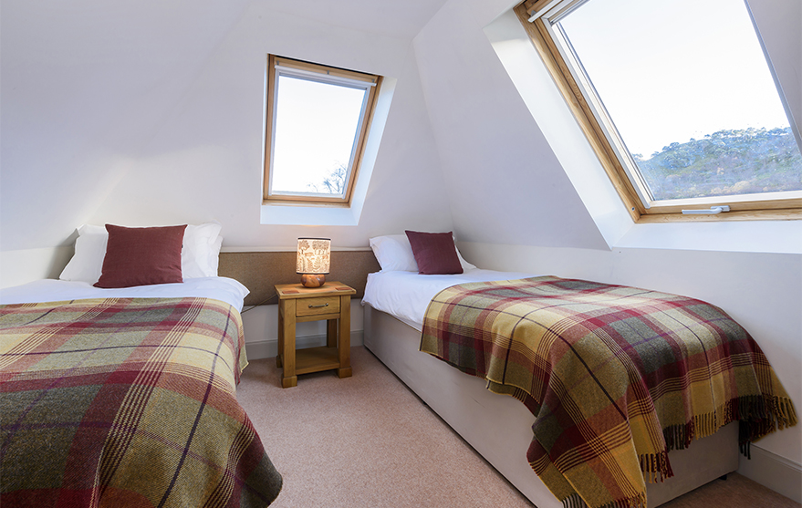 Bedroom with two single beds and Velux windows, alongside a bedside table with lamp.